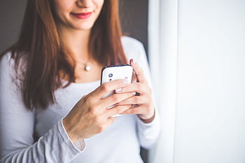 Young woman interacting with a smart near a window, showcasing modern communication technology. HD wallpaper