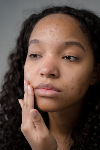 A thoughtful woman with curly hair examines her skin condition during a skincare routine. HD phone wallpaper
