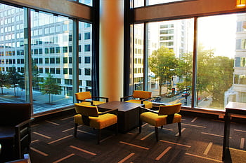 Contemporary hotel lounge featuring yellow chairs and cityscape view through large windows. HD wallpaper