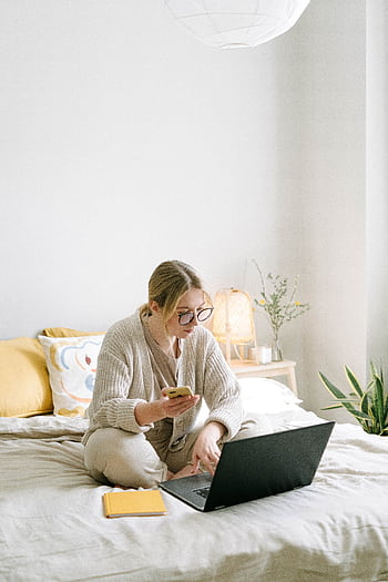 A woman working remotely from home sitting on a bed using a laptop and in a cozy bedroom. HD phone wallpaper