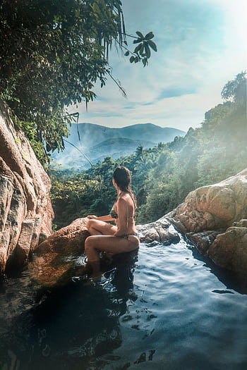 A woman in a swimsuit relaxes by a waterfall with lush mountains in Ko Samui, Thailand. HD phone wallpaper