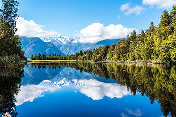 Peaceful mountain lake with stunning reflections and surrounding forest on a clear day. HD wallpaper