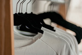 Close-up of white t-shirts hanging neatly on black hangers in a minimalist indoor closet setting. HD wallpaper