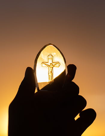 A silhouetted hand holds a crucifix against a vibrant sunset sky, symbolizing faith and spirituality. HD phone wallpaper