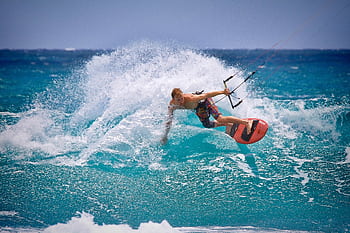 Thrilling kitesurfing moment captured as a surfer rides the waves in vibrant ocean waters. HD wallpaper