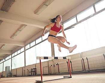 A female athlete demonstrates agility and grace by jumping a hurdle indoors. HD wallpaper