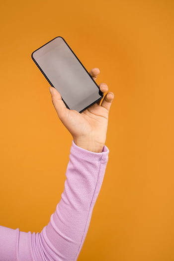 Close-up of a hand holding a smart against an orange background. HD phone wallpaper