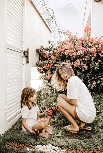 A mother and daughter bond in a vibrant garden filled with flowers, enjoying leisure time. HD phone wallpaper