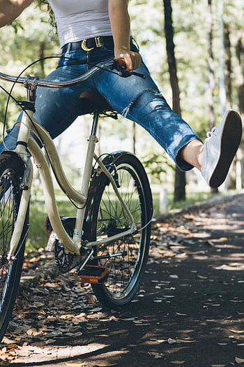 A woman enjoys a relaxing bike ride through a sunlit park path. HD phone wallpaper