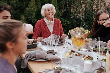 Happy elderly woman laughs with family during an outdoor meal. HD wallpaper