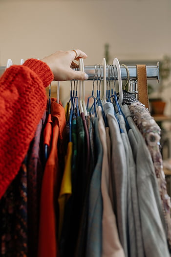 A woman browsing garments on hangers in a retail clothing store. HD phone wallpaper