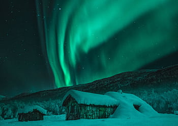 Captivating view of Northern Lights illuminating snowy cabins and wintry night sky in Norway. HD wallpaper