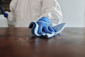 Person in protective suit using disinfectant on surface to ensure cleanliness and safety. HD wallpaper