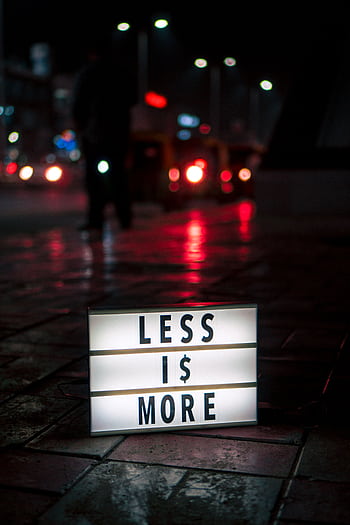 Minimalist lightbox sign reading 'Less is More' on a wet street at night, New Delhi. HD phone wallpaper