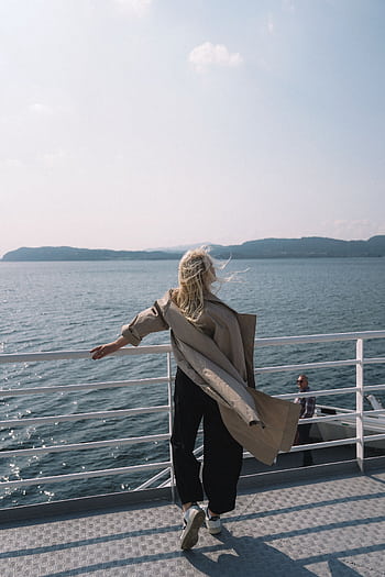 A woman stands on a ferry overlooking the ocean, enjoying a serene moment of relaxation in Norway. HD phone wallpaper