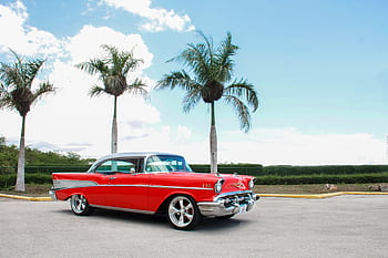 A classic red Chevrolet parked outdoors against a blue sky with palm trees. HD wallpaper