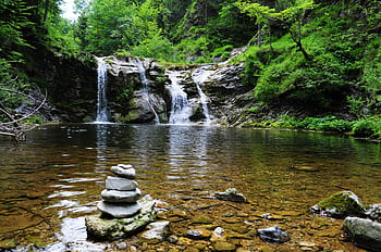 Peaceful forest waterfall with serene stone cairn, ideal for nature and travel themes. HD wallpaper
