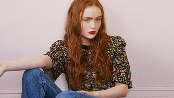Actress Redhead Sadie Sink Is Sitting In Light Pink Wall Background Wearing Colorful Flowers Printed Black Top And Blue Jeans Girls HD wallpaper