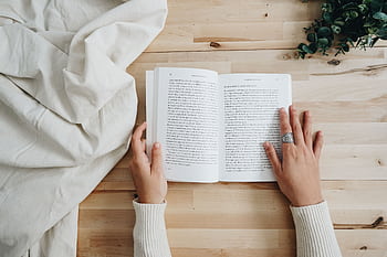 Top view of a person reading a book on a wooden table with a cozy setup, ideal for leisure and learning concepts. HD wallpaper