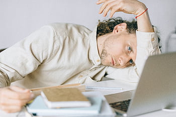 A tired Caucasian man at a desk, showing signs of exhaustion and stress, exemplifying workplace burnout. HD wallpaper