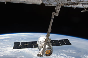 View of a spacecraft docked at the ISS above Earth with visible solar panels. HD wallpaper