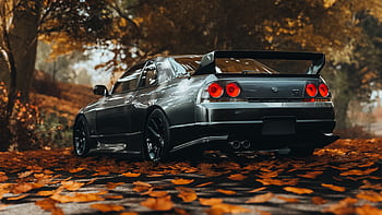 A sleek Nissan Skyline GTR R33 captured amidst vibrant autumn leaves, showcasing its sporty design. HD wallpaper