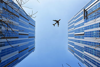 A striking low angle shot capturing skyscrapers and an airplane above a clear blue sky. HD wallpaper