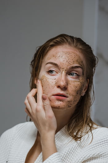 Young woman applying a natural coffee scrub to her face as part of her skincare routine. HD phone wallpaper
