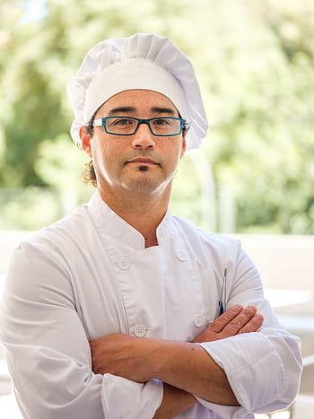 Professional male chef wearing glasses and toque blanche, standing confidently with crossed arms. HD phone wallpaper
