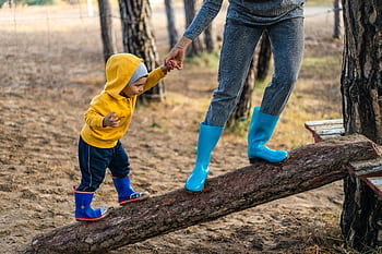 A woman helps her toddler walk on a log in a park, showcasing child support and family bonding. HD wallpaper