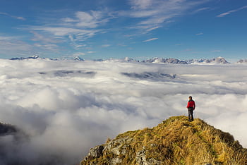 A lone hiker stands atop a mountain peak surrounded by clouds, embracing nature's beauty. HD wallpaper
