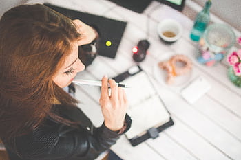 Overhead view of a young woman studying at a home office desk, thinking and taking notes. HD wallpaper