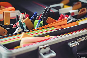 A collection of colorful office supplies neatly arranged in a suitcase, perfect for professionals on the go. HD wallpaper