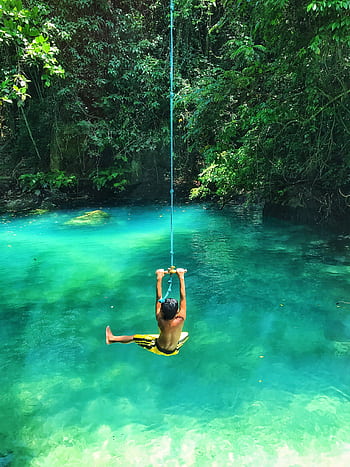 A child swinging joyfully on a rope over a stunning turquoise tropical lagoon. HD phone wallpaper