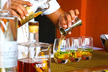 A bartender expertly pours cocktails in glasses on a bar counter. HD wallpaper