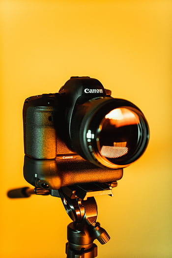 Close-up of a DSLR camera mounted on a tripod with an orange backdrop, highlighting graphy equipment. HD phone wallpaper