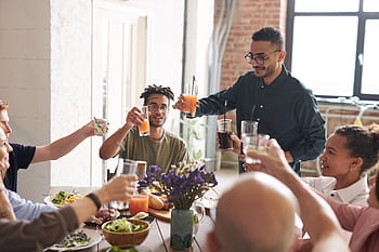 Group of friends toasting drinks during a lively indoor meal, enjoying togetherness and celebration. HD wallpaper