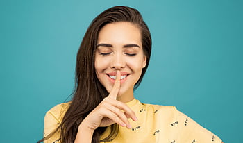 Charming woman with finger on lips, signaling silence against a teal background. HD wallpaper