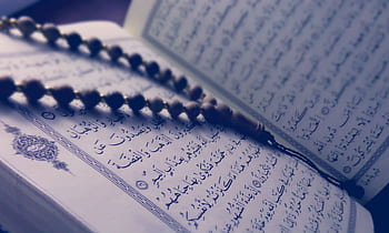 A close-up of prayer beads resting on an open Quran page, depicting Islamic faith and worship. HD wallpaper