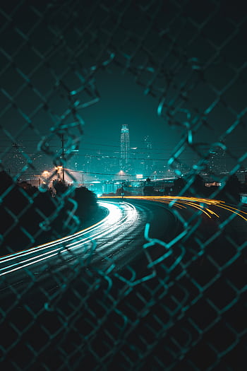 Captivating long exposure night shot of San Francisco skyline through a fence, featuring vibrant light trails. HD phone wallpaper