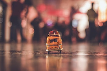A nostalgic yellow toy van with luggage, reflecting on a city street during sunset. HD wallpaper