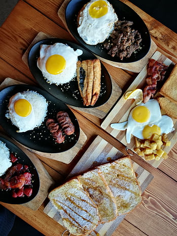 An appetizing breakfast spread featuring eggs, meats, toast, and rice on a wooden table. HD phone wallpaper
