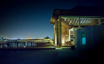 A modern waterfront house illuminated at night, featuring a serene cityscape and reflection on water. HD wallpaper