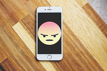 A smart showing an angry emoticon rests on a wooden table, emphasizing tech and emotion. HD wallpaper