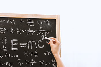 Close-up of hand writing physics equations on a chalkboard indoors. HD wallpaper