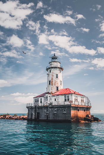 Beautiful rustic lighthouse surrounded by ocean waters under a bright summer sky. HD phone wallpaper