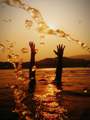 Silhouetted hands reach skyward in a golden sunset, reflecting on rippling water. HD phone wallpaper