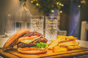 Delicious cheeseburger with lettuce and fries on a wooden board, perfect for a fast food meal. HD wallpaper