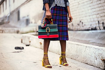Fashion-forward outfit with plaid skirt and colorful handbag in urban setting. HD wallpaper
