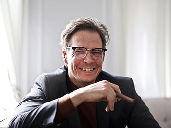 Cheerful businessman in glasses and suit holding a cigar, indoors. HD wallpaper